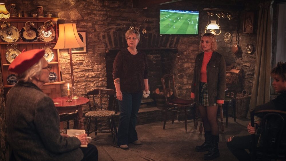 Three white women are in a dimly lit brick pub; they look concerned.