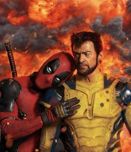 Ryan Reynolds' Deadpool, wearing a red spandex costume with large black egg-shaped eyes and black shoulder pads, embraces a suspicious-looking Hugh Jackman's Kim. Wolverine is a white man with short brown hair, ear-like spikes, and mutton chops blended with a neatly trimmed beard and goatee.