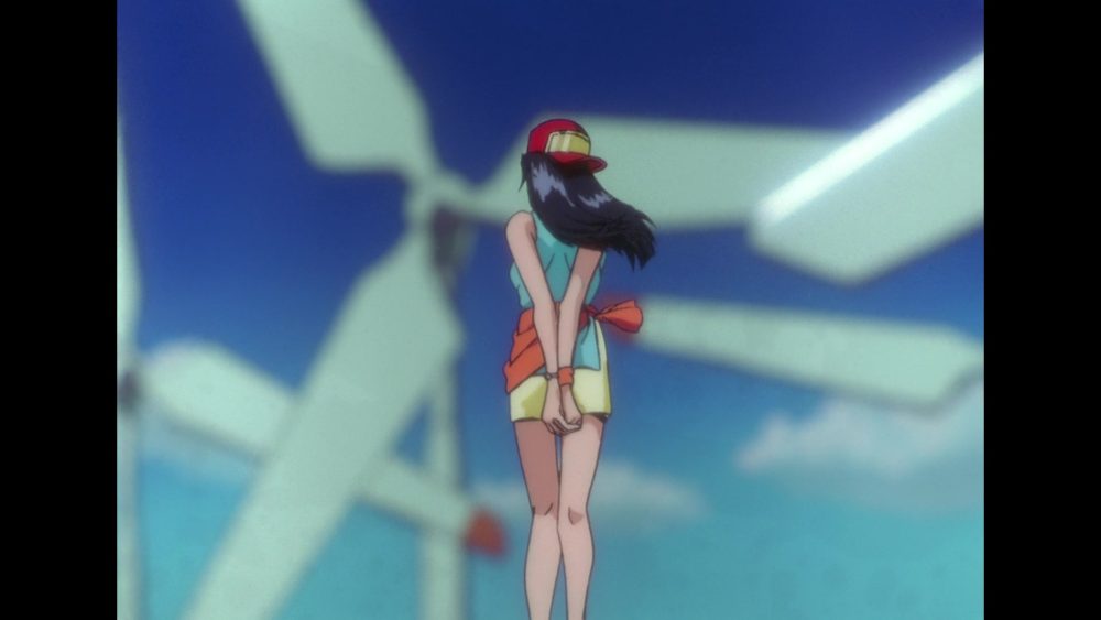 Macross Plus. A young woman wearing a hat and a jacket tied around her waist looks away from the viewer toward the white wind turbines.