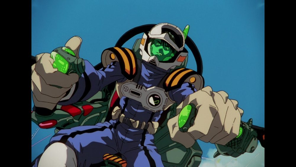 Macross Plus. Man sits in the cockpit of an experimental fighter jet. He wears blue and chrome fighter gear with green clear panels.