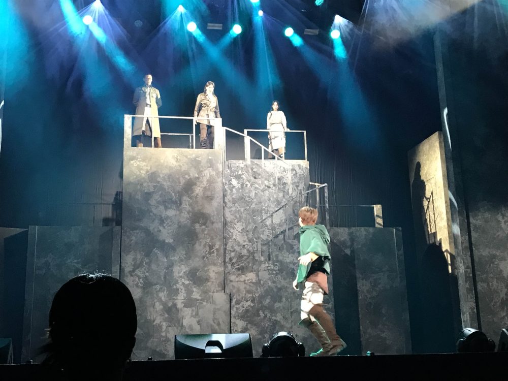 In Attack on Titan the Musical, Eren looks up at his mentor, father, and mother, who are also looking down at him from the top of the scene