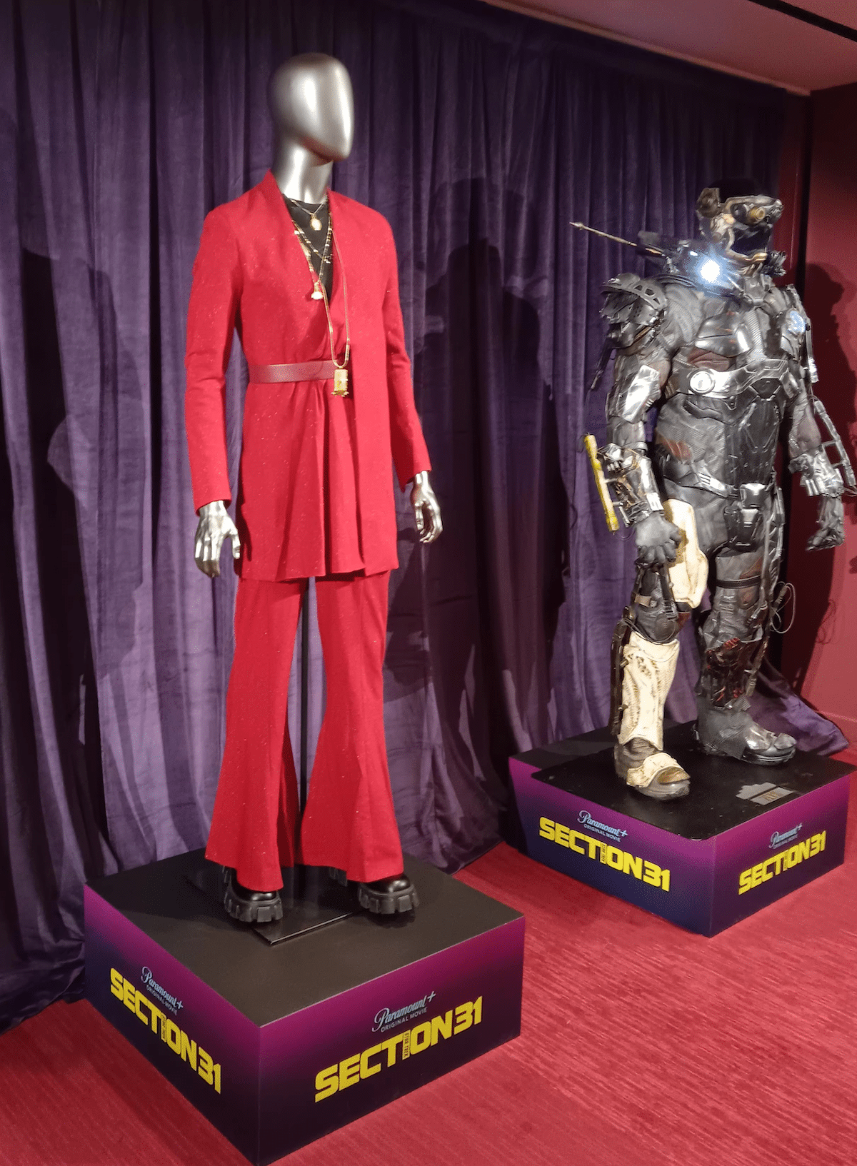 Two costumes on mannequins atop Section 31 pedestals. The left is red and made of fabric, worn by Fuzz's Vulcan conveyance; on the right is a mechanical suit worn by Zeph. 