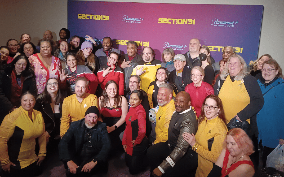 A group of people, many in Star Trek uniforms, standing in front of a Section 31 backdrop.